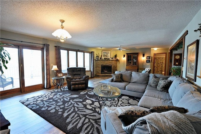 living area featuring ceiling fan with notable chandelier, a fireplace with raised hearth, a textured ceiling, and wood finished floors