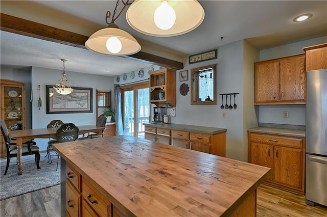 kitchen featuring butcher block countertops, wood finished floors, freestanding refrigerator, brown cabinetry, and hanging light fixtures