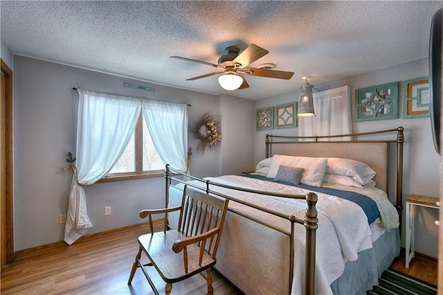 bedroom featuring ceiling fan, a textured ceiling, baseboards, and wood finished floors