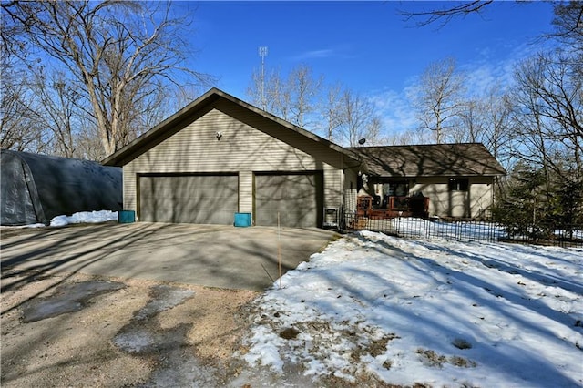 view of snow covered exterior with concrete driveway, a garage, and fence