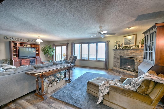 living area featuring a stone fireplace, a textured ceiling, wood finished floors, and ceiling fan