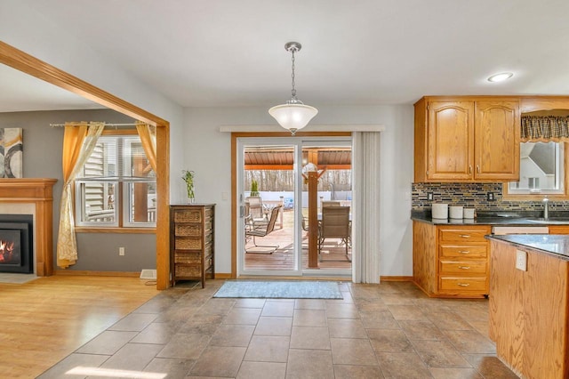 kitchen featuring a fireplace with flush hearth, dark countertops, decorative backsplash, baseboards, and hanging light fixtures