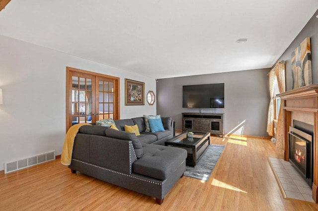 living area with light wood-type flooring, visible vents, a tiled fireplace, and french doors