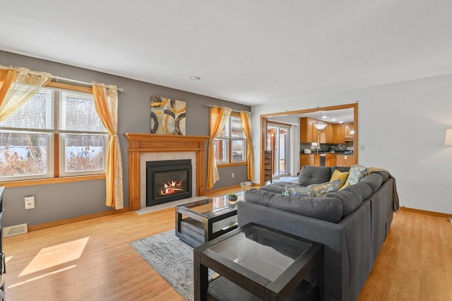 living room with a fireplace with flush hearth, baseboards, and light wood-type flooring