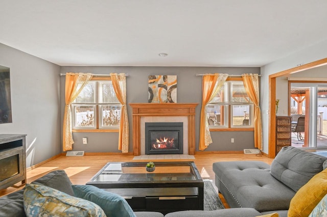 living room featuring visible vents, a fireplace with flush hearth, and wood finished floors