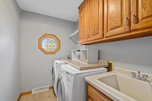 laundry room with visible vents, washer and clothes dryer, a sink, cabinet space, and light wood finished floors