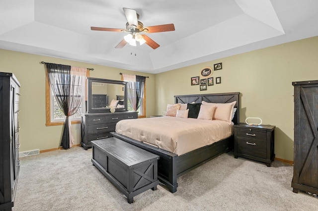 bedroom featuring a ceiling fan, baseboards, visible vents, a tray ceiling, and light colored carpet