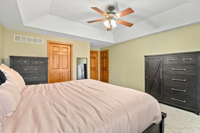 carpeted bedroom with visible vents, ceiling fan, and a tray ceiling