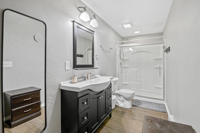 bathroom with wood finish floors, toilet, a shower stall, baseboards, and vanity