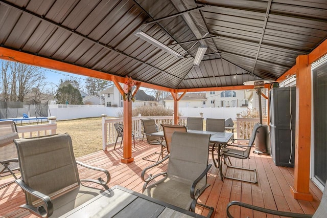 wooden terrace with a trampoline, a gazebo, a lawn, a fenced backyard, and outdoor dining space