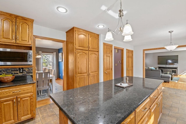 kitchen featuring a notable chandelier, dark stone countertops, stainless steel microwave, tasteful backsplash, and a kitchen island