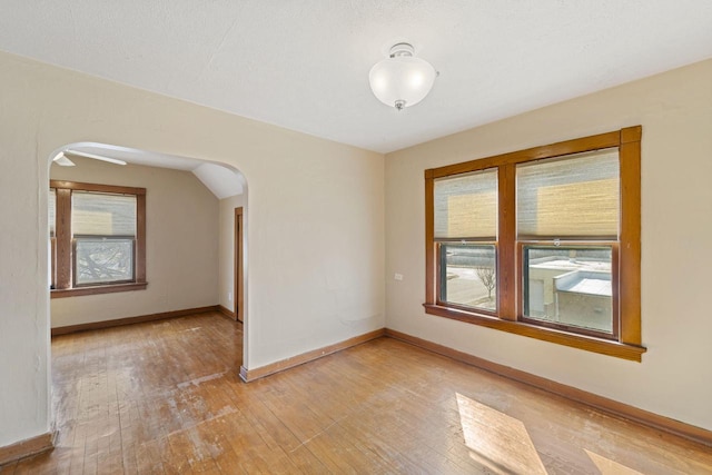 unfurnished room with arched walkways, a healthy amount of sunlight, and light wood-style flooring