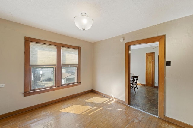 empty room featuring a textured ceiling, baseboards, and light wood-style floors