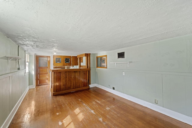 interior space with visible vents, wainscoting, a textured ceiling, and hardwood / wood-style flooring