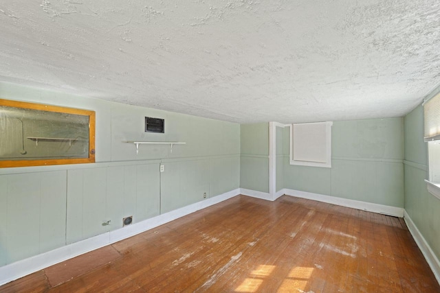 unfurnished room with visible vents, a wainscoted wall, a textured ceiling, and hardwood / wood-style floors