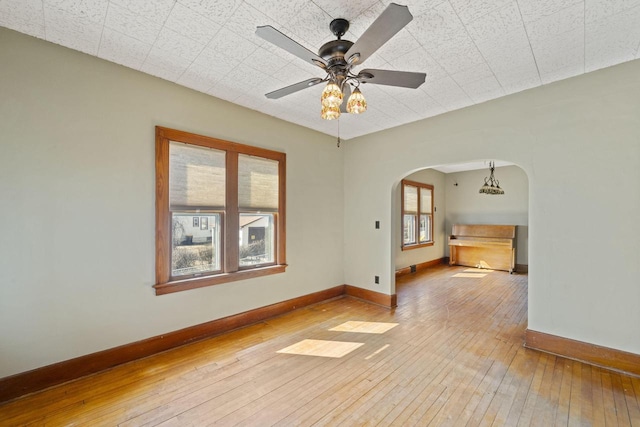 empty room with baseboards, arched walkways, wood-type flooring, and a ceiling fan