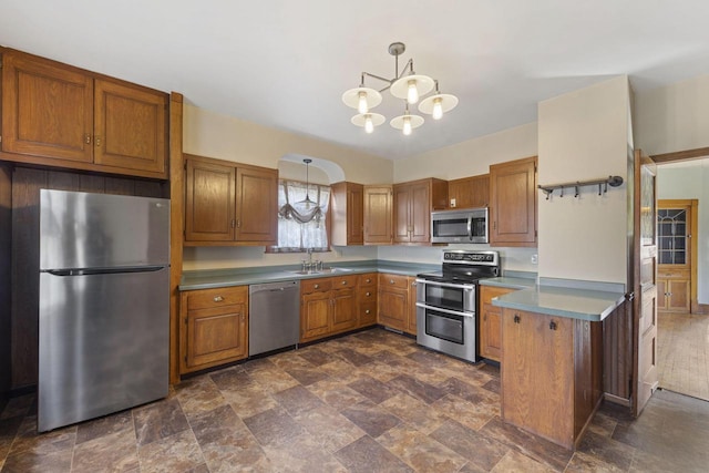 kitchen featuring brown cabinets, a notable chandelier, a sink, stone finish flooring, and appliances with stainless steel finishes