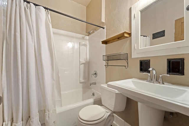 full bath with a sink, shower / bathtub combination with curtain, toilet, and a textured wall