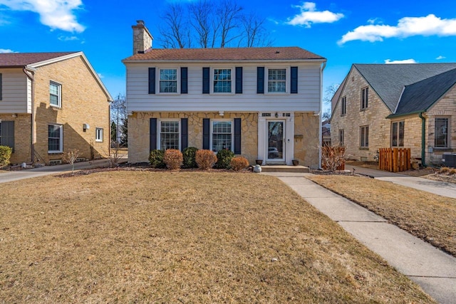 colonial home with stone siding, a front lawn, and a chimney