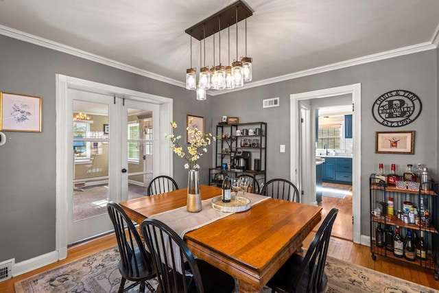 dining room with light wood-type flooring, baseboards, visible vents, and ornamental molding