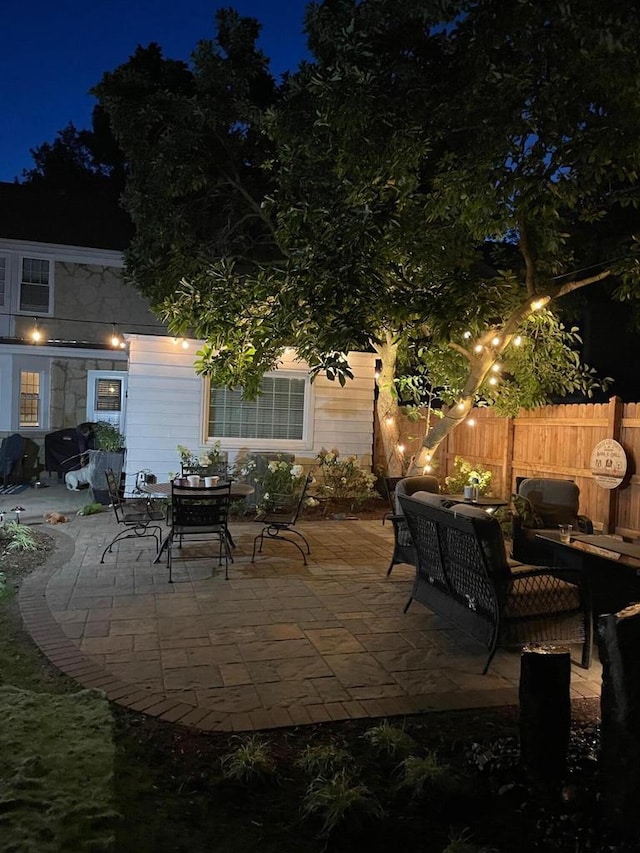 patio at night featuring grilling area, outdoor lounge area, and fence