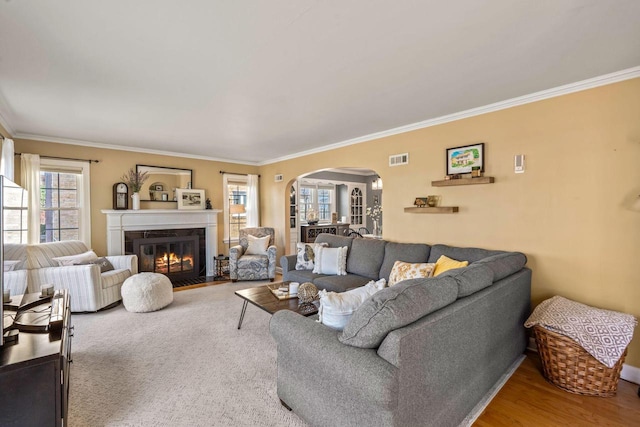 living area featuring a fireplace with flush hearth, visible vents, arched walkways, and ornamental molding