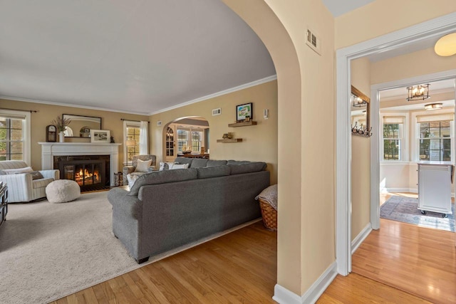 living area featuring a glass covered fireplace, wood finished floors, arched walkways, crown molding, and baseboards