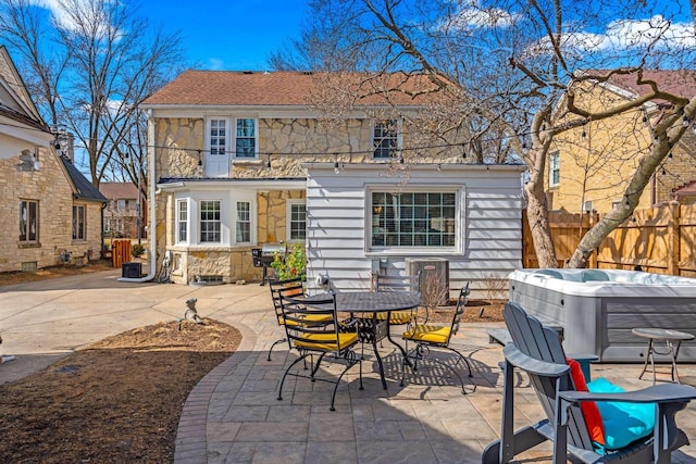 rear view of property featuring outdoor dining space, a patio, fence, a hot tub, and stone siding