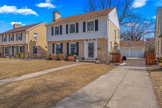 colonial house featuring a detached garage, a front yard, a chimney, an outbuilding, and stone siding