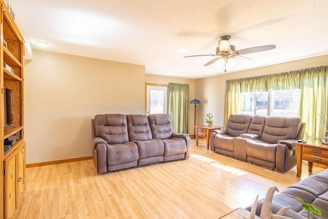 living area featuring a ceiling fan, baseboards, light wood finished floors, and a textured ceiling