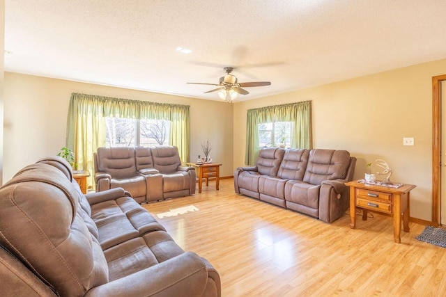 living room with a textured ceiling, light wood-style flooring, baseboards, and ceiling fan