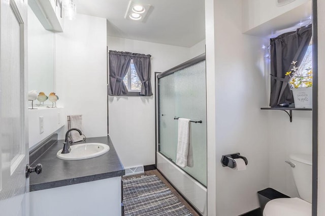 bathroom featuring vanity, toilet, visible vents, and combined bath / shower with glass door