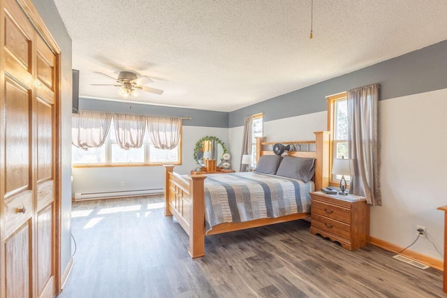 bedroom featuring a baseboard heating unit, a textured ceiling, visible vents, and wood finished floors