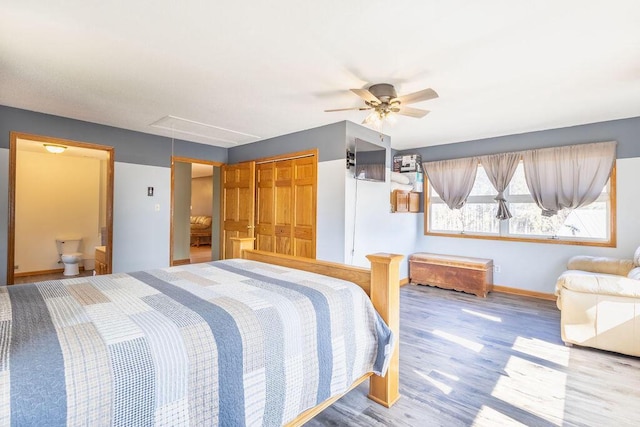 bedroom featuring wood finished floors, baseboards, attic access, ceiling fan, and ensuite bathroom