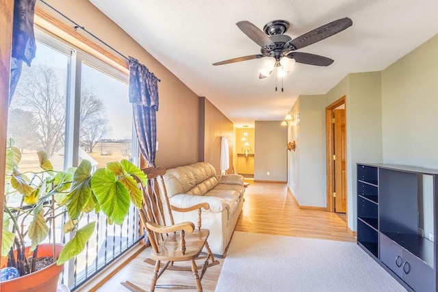 living area featuring baseboards, light wood-type flooring, and a ceiling fan