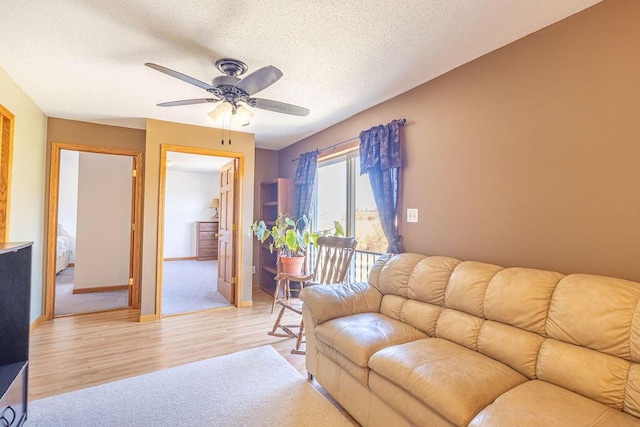 living area featuring a textured ceiling, light wood-style flooring, baseboards, and ceiling fan