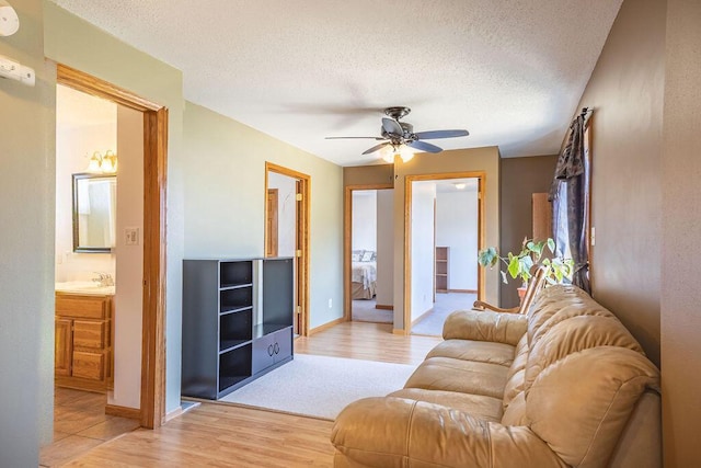 living room with a textured ceiling, baseboards, light wood finished floors, and ceiling fan