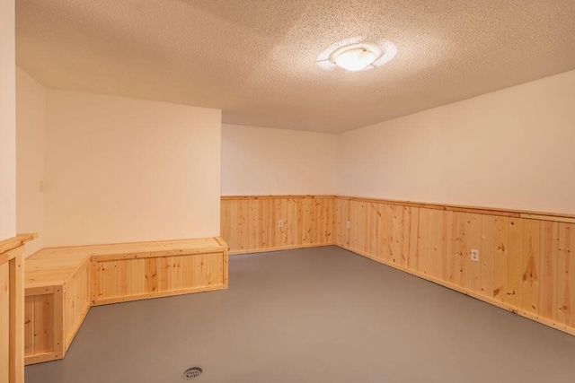 spare room featuring a textured ceiling, concrete floors, and wainscoting