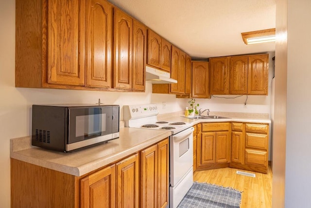 kitchen with brown cabinetry, white electric stove, a sink, under cabinet range hood, and stainless steel microwave