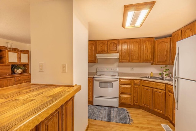 kitchen with white appliances, brown cabinetry, visible vents, and under cabinet range hood