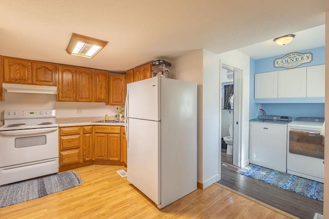 kitchen featuring washer and clothes dryer, under cabinet range hood, a sink, white appliances, and light wood-style floors