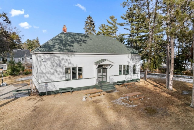 view of front of home featuring entry steps, a chimney, and a shingled roof