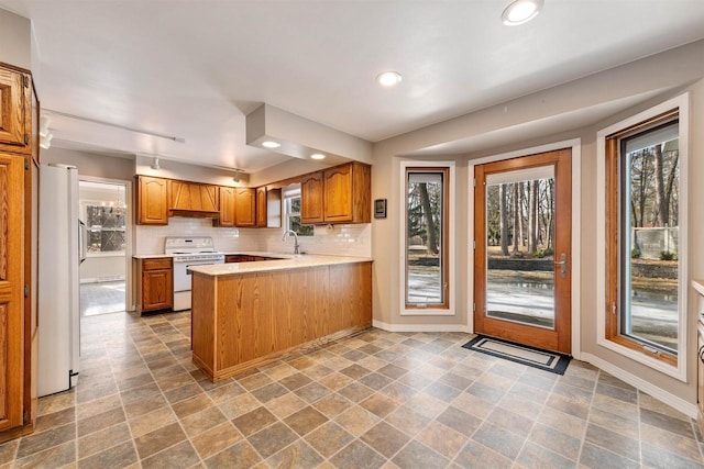 kitchen with decorative backsplash, a peninsula, brown cabinetry, white appliances, and a sink