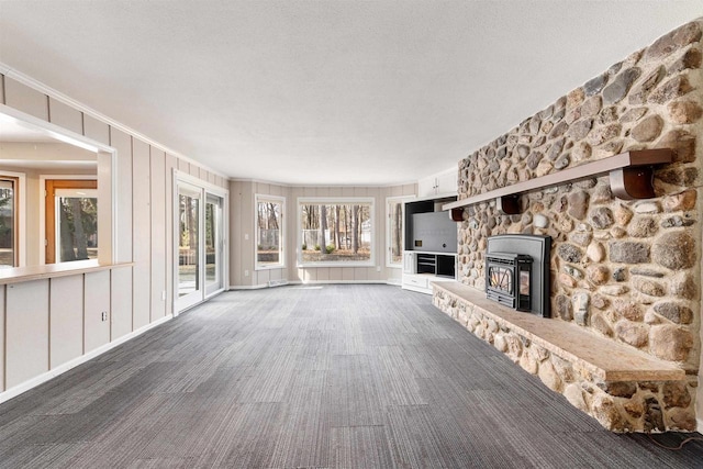 unfurnished living room featuring a textured ceiling, a decorative wall, carpet floors, and ornamental molding