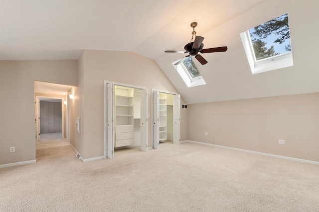 unfurnished bedroom featuring lofted ceiling with skylight, light colored carpet, two closets, and baseboards