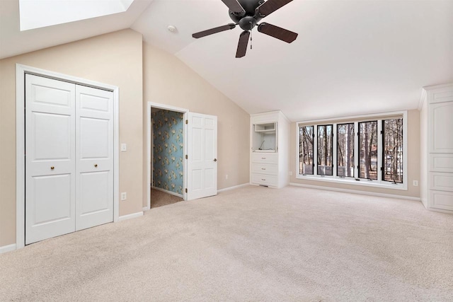 unfurnished bedroom featuring lofted ceiling with skylight, ceiling fan, baseboards, and carpet