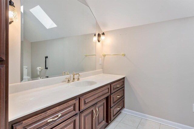 bathroom with tile patterned floors, toilet, vaulted ceiling with skylight, baseboards, and vanity