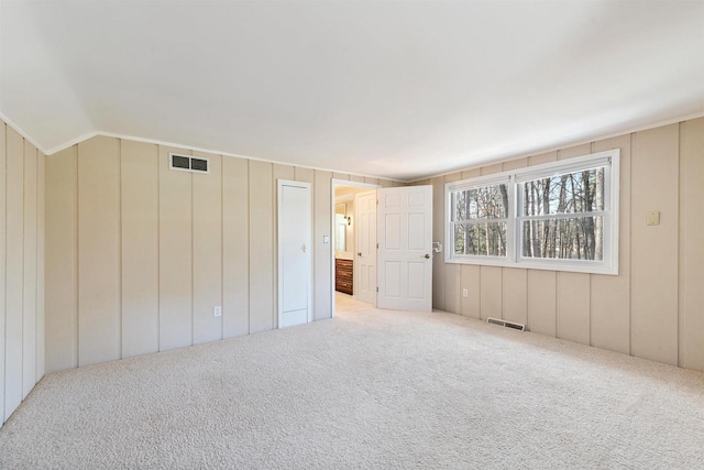 unfurnished bedroom with visible vents, carpet floors, a decorative wall, and vaulted ceiling