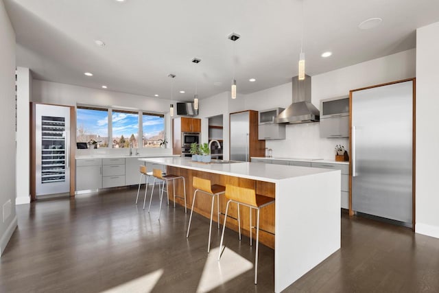 kitchen with modern cabinets, a sink, wall chimney range hood, a spacious island, and light countertops