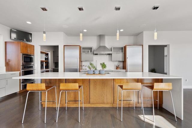 kitchen with dark wood-style flooring, light countertops, built in appliances, wall chimney range hood, and modern cabinets